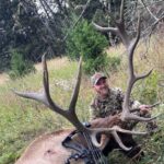 A man poses with an Elk he took down while hunting at Elk Ridge Outfitters