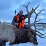 A man poses with the elk he took down at Elk Ridge Outfitters