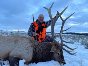 A man poses with the elk he took down at Elk Ridge Outfitters